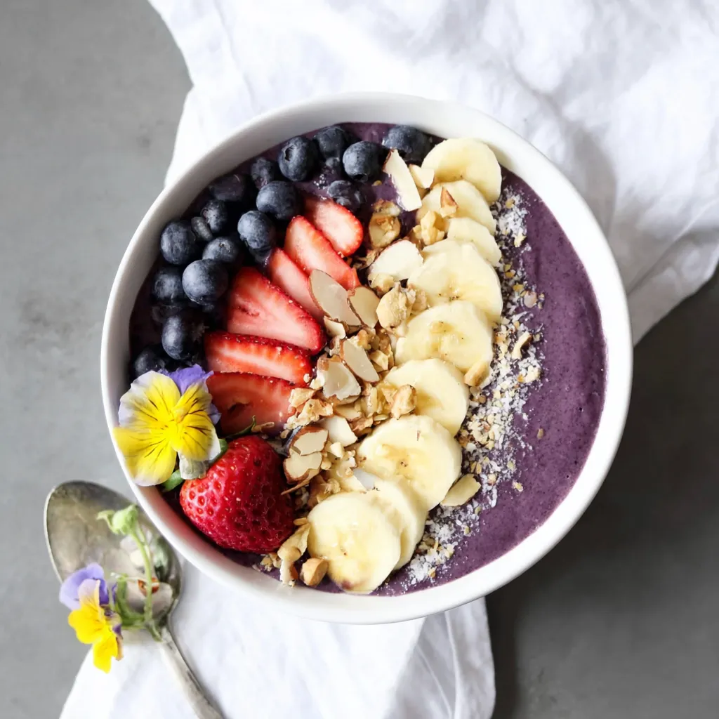 Acai smoothie bowl topped with sliced banana, fresh strawberries, blueberries, granola, nuts and shredded coconut, served in a white bowl