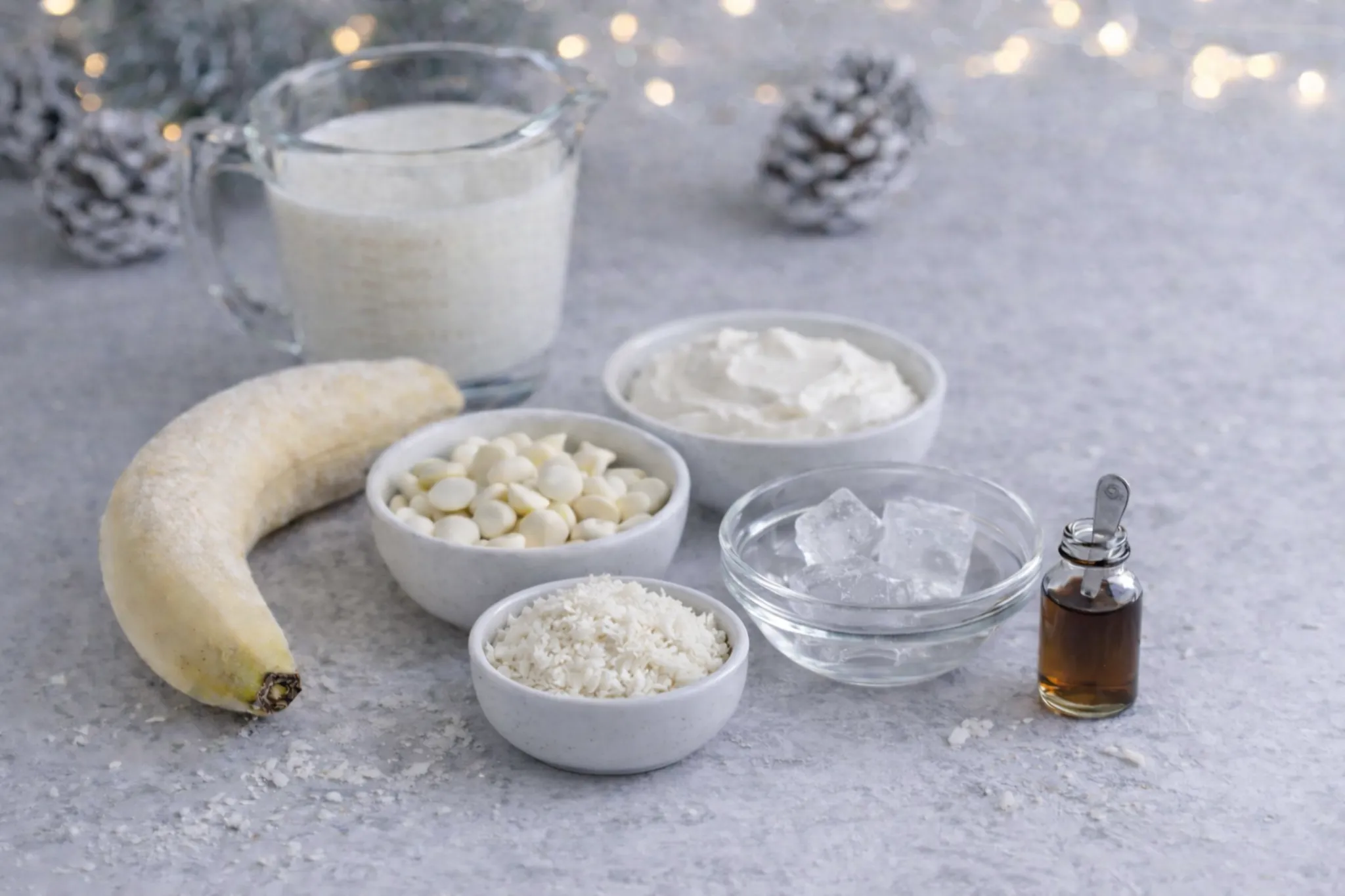Ingredients for Winter Wonderland Smoothie including banana, Greek yogurt, milk, white chocolate chips, shredded coconut, ice cubes and vanilla extract
