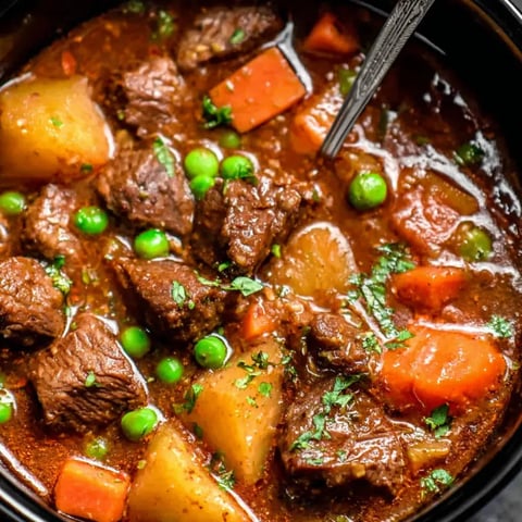 A close up of a beef stew with peas and carrots.