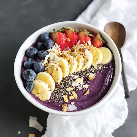 Acai bowl topped with banana slices, strawberries, blueberries, granola and coconut flakes
