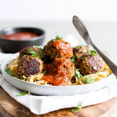 Baked lentil meatballs served over spaghetti with tomato sauce in a white bowl