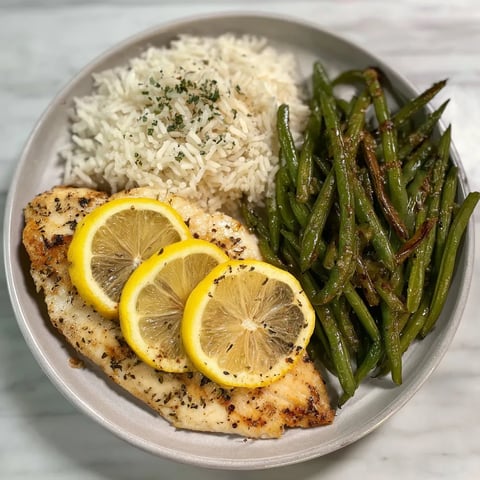 Lemon Garlic Butter Tilapia served with jasmine rice and roasted green beans topped with fresh lemon slices in a bowl